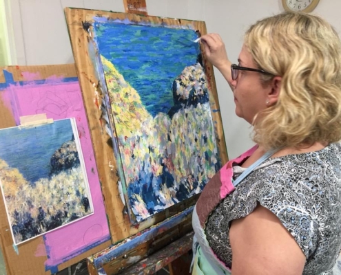 A woman with short hair paints a landscape on a canvas with a palette knife