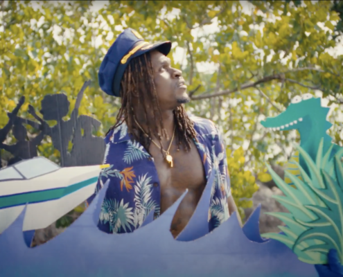 Boat, wave papercut out in front of a Black man in a boat captain hait with a blue floral shirt thats open