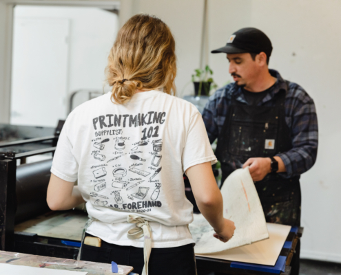 Two people holding a large sheet of paper in a printmaking studio