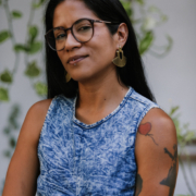 Diana Larrera Headshot Diana Larrera in a blue tank in front of a wall covered in viney plants