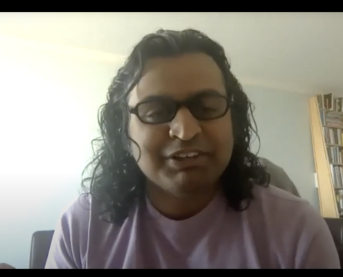 Alpesh Patel in a lilac t shirt with shoulder length hair