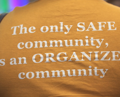 A person wearing an orange T-shirt with text on the back that reads The only SAFE community is an organized community