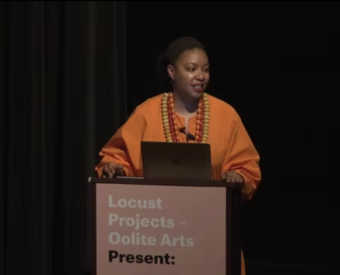 Adrienne Edwards in orange standing behind a podium