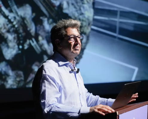 Paul Schimmel in a blue button down in front of a podium standing in front of a projected image