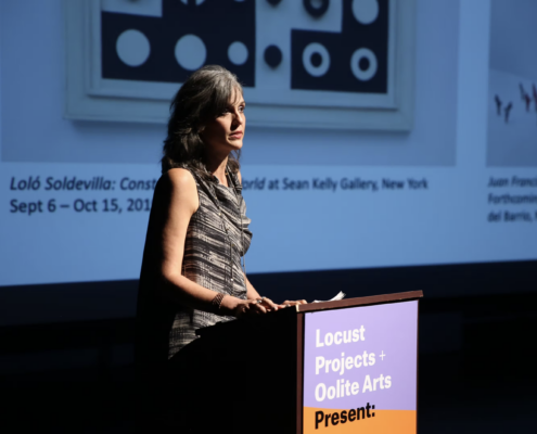 Olga Viso standing at a podium in front of a projected art work