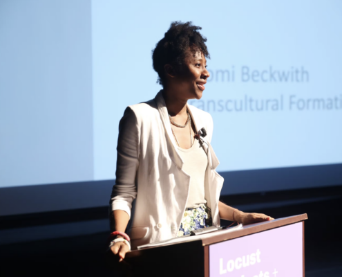 Naomi Beckwith in white standing at a podium