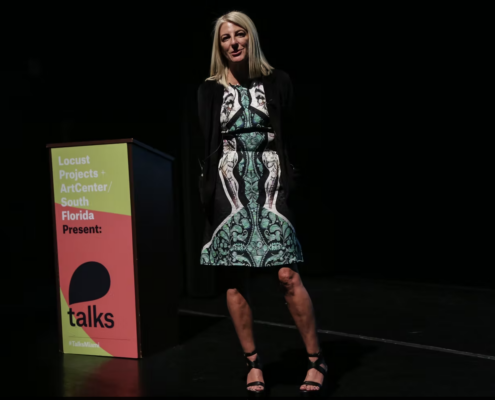 Heidi Zuckerman standing next to a Talks branded podium in a patterned white and green dress