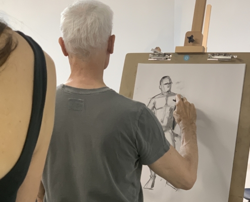 Gray Haired person facing away from the camera drawing on an easel