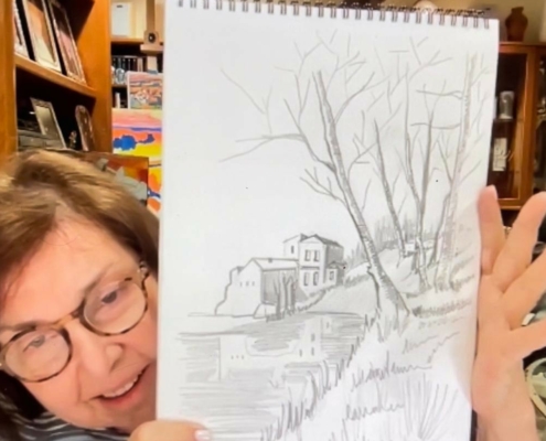 Person holding a sketch pad with a drawing of trees and a house