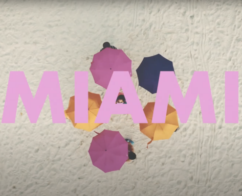 The word Miami in pink on top of various pink and yellow umbrellas on sand