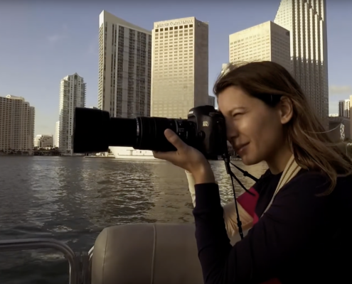 Anastasia Samoylova looks through a telephotolens with the water and city in the background.